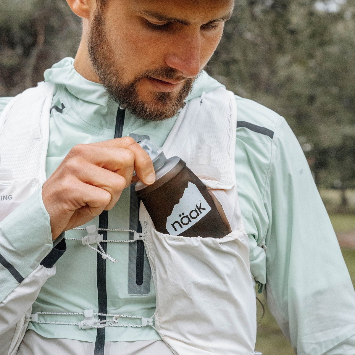 Man holding from the naak soft flask outdoors with trees in the background