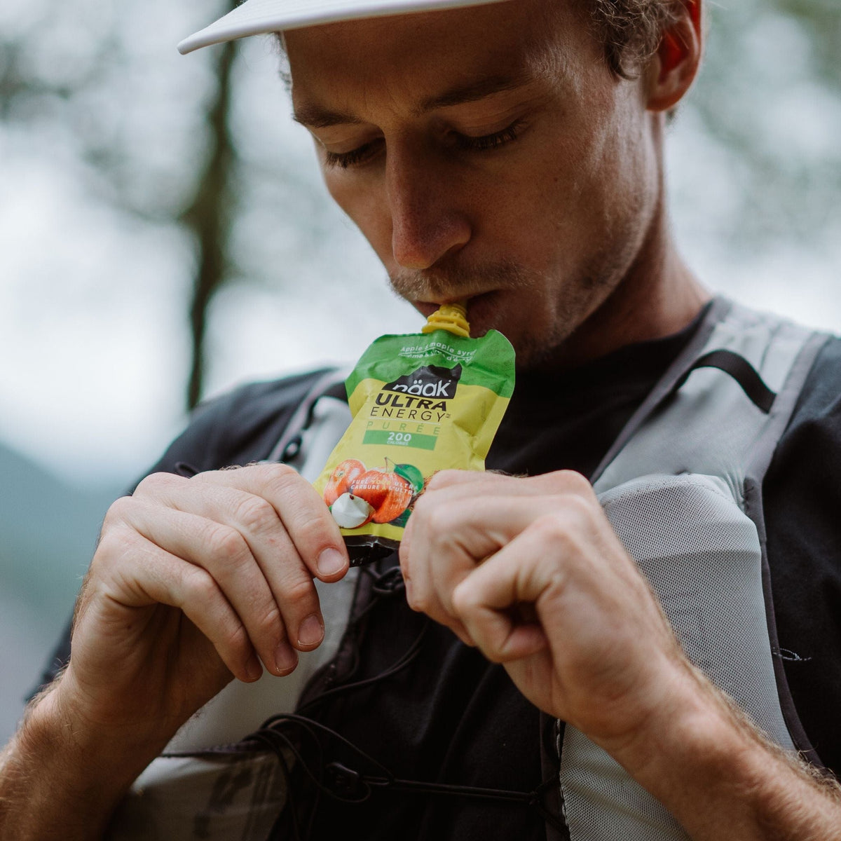 Man outdoors eating a naak ultra energy puree apple maple syrup with a blurred natural background